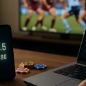Laptop and smartphone with soccer game on TV in background